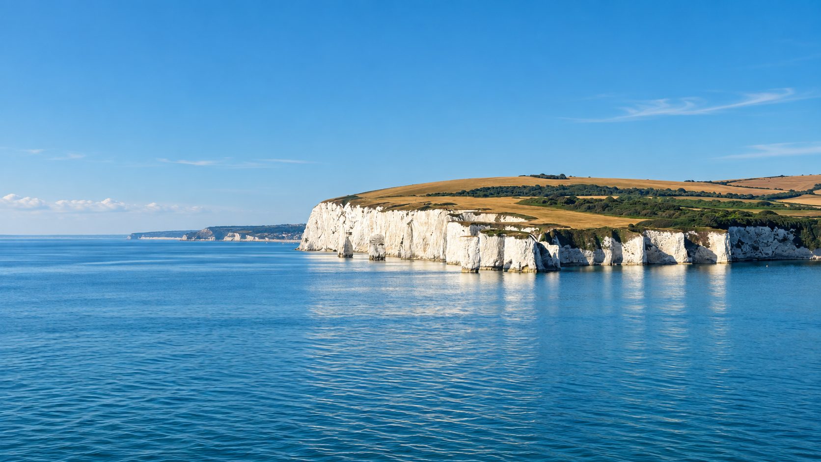 A long line of white chalk cliffs receding into the distance above calm blue water.