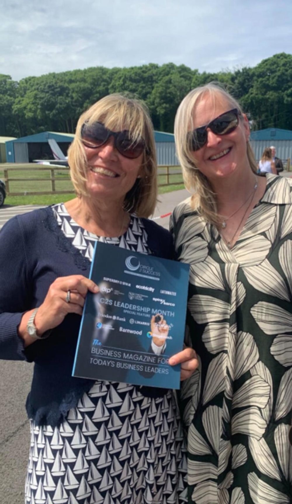 Sarah outdoors at an event, holding a business magazine with a colleague.