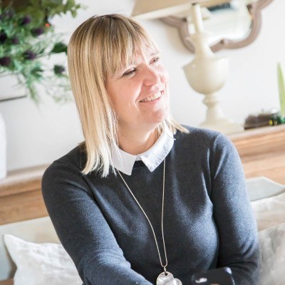 Sarah Taylor Phillips sitting indoors in a blue jumper, laughing at something off camera.