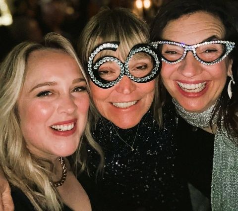 Sarah Taylor Phillips laughing with two friends, wearing novelty glasses shaped like a sixty.
