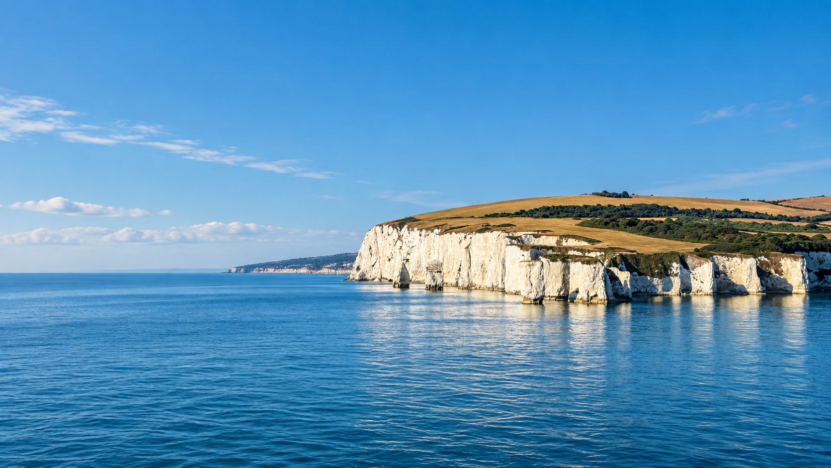 A long line of chalk cliffs above still water, late light on the fields above.