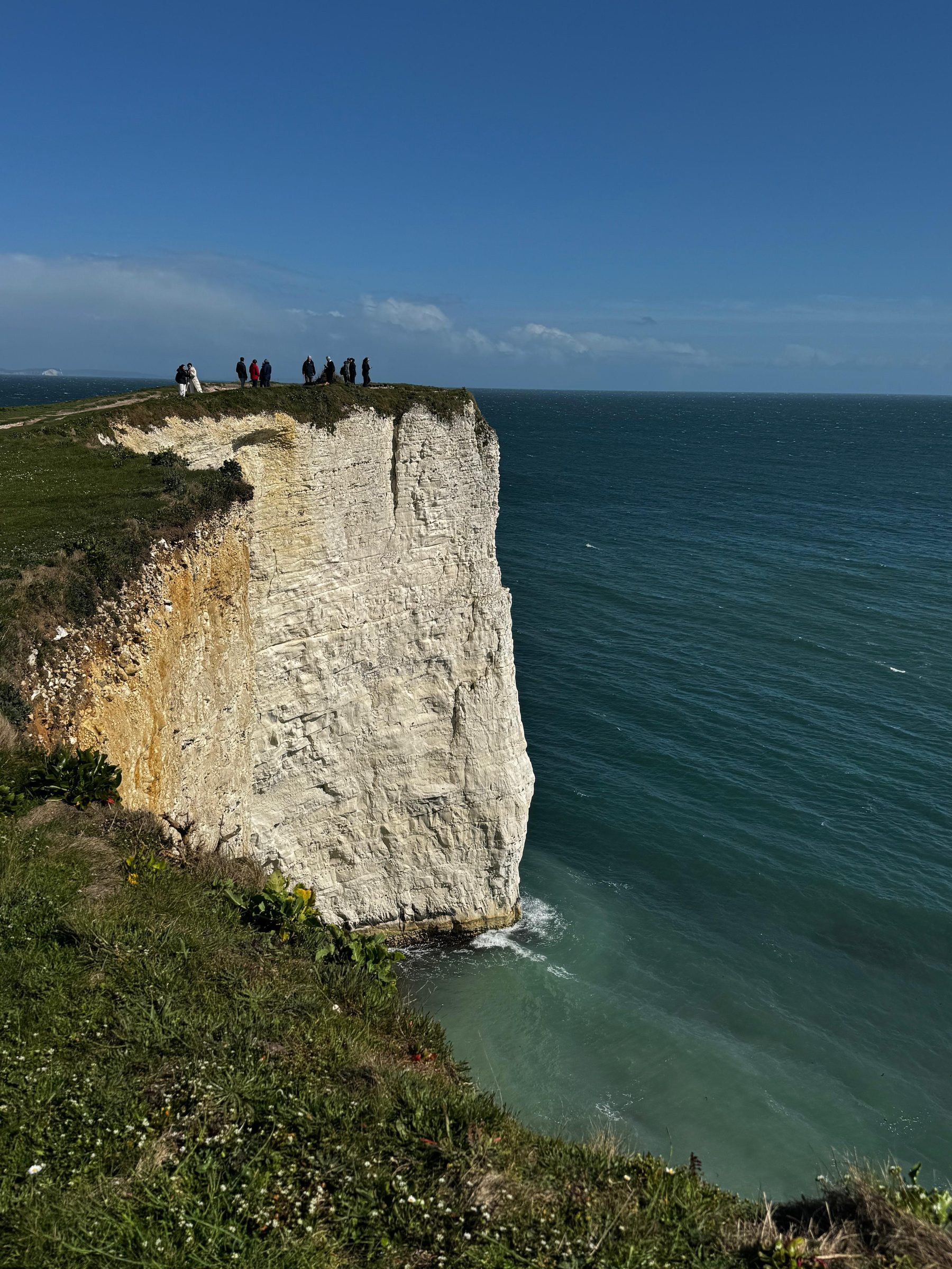 Chalk cliffs and a sea stack, with people standing at the clifftop above.