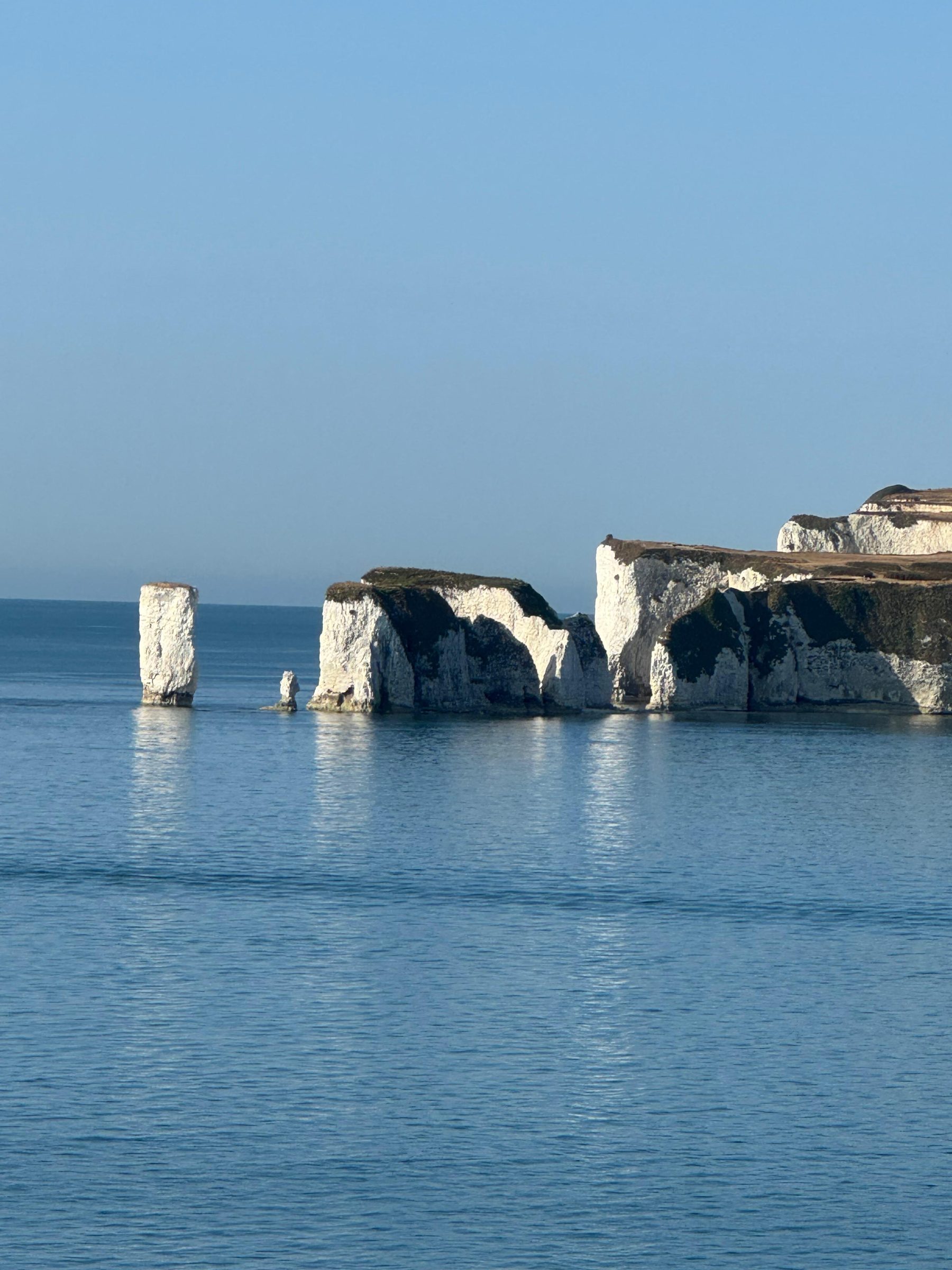 Chalk stacks of different heights standing in open blue water below a headland.