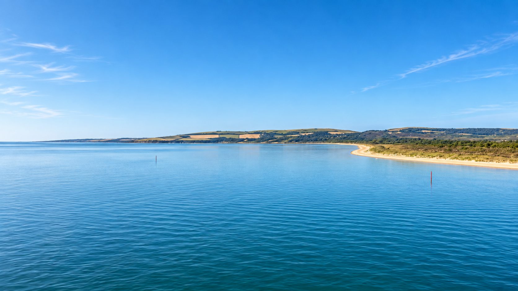 A wide, calm bay with a long sand spit and low green hills beyond.